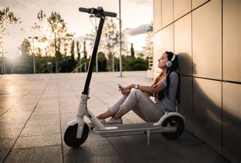 Femme détendue assise contre un mur avec une trottinette électrique, illustrant un usage urbain pour débutants